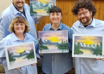 4 people showing off their new Bob Ross paintings